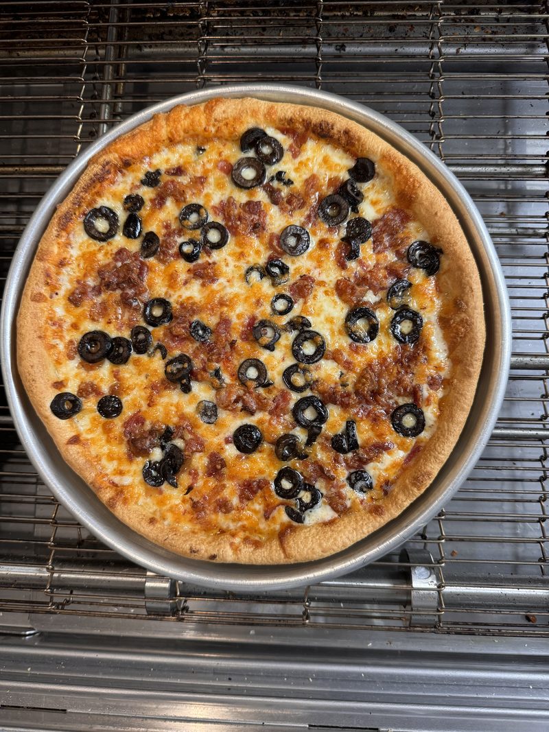 A bacon and black olive pizza on the rack